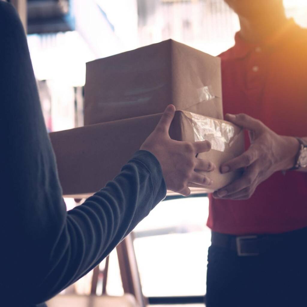 Close-up of a delivery service worker handing over packages to a customer indoors.