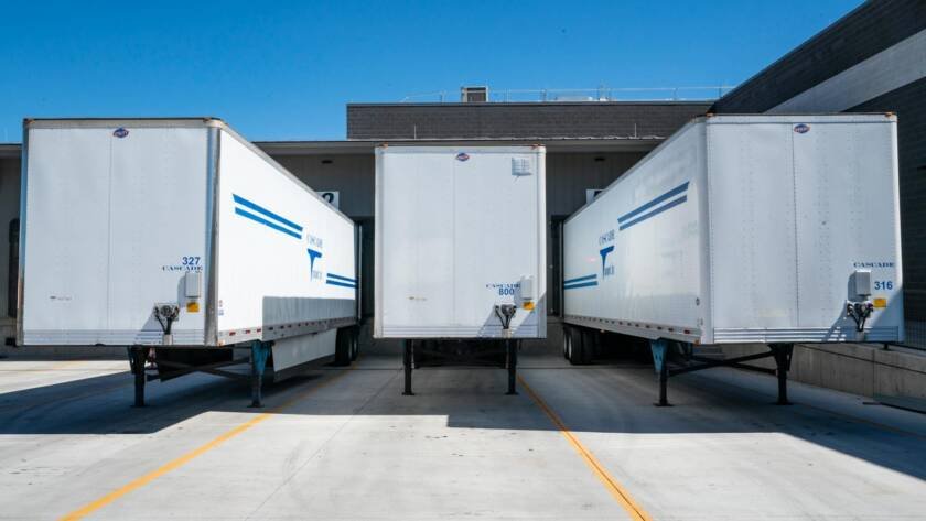 Three white cargo trailers parked at an industrial shipping dock under clear blue skies.