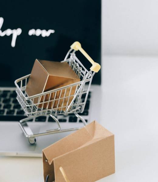 A miniature shopping cart with a parcel on a laptop symbolizes online shopping and e-commerce.