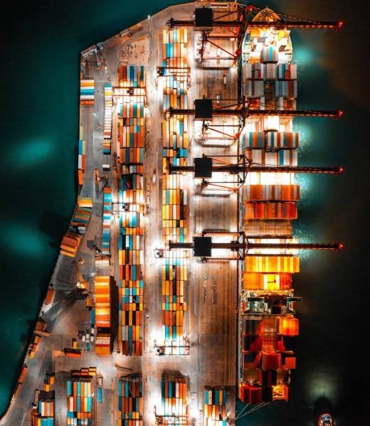 Dramatic aerial view of a busy shipping port with colorful containers and bright lights at night.
